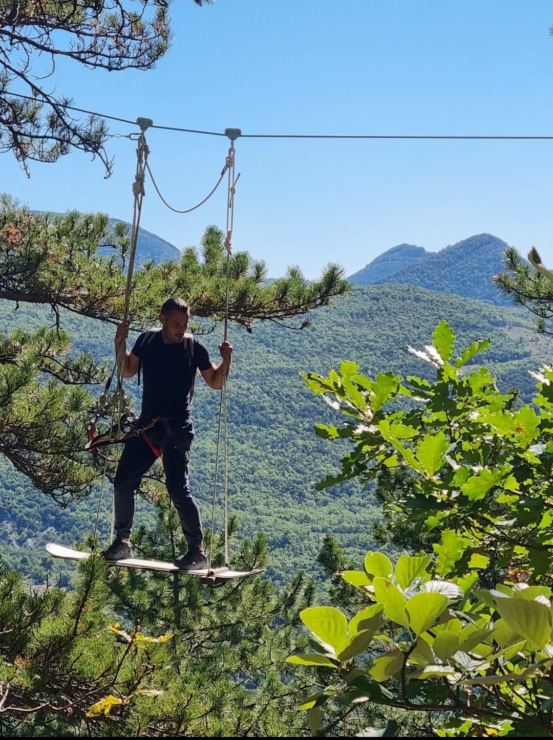 Un Aspirant Chevalier 🛡️ se laisse glisser en toute légèreté sur l'obstacle du surf du parcours noir "L'Échelle du Donjon". La photo capture ce moment de plaisir face au panorama des collines environnantes ⛰️. aaccrobranche Nyons