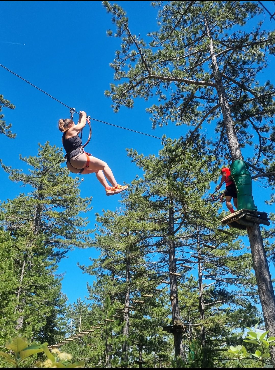 Au début du parcours bleu "Le Seigneur des Bois" à l'accrobranche de Nyons, une châtelaine s'élance sur la tyrolienne tandis qu'un aventurier s'engage sur le pont suspendu.